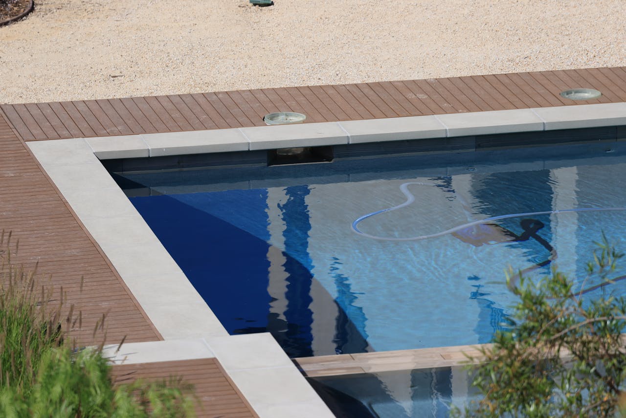A serene swimming pool with wooden decking and clear blue water on a sunny day.