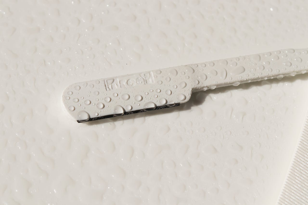 Detailed close-up image of a white razor covered in water droplets on a white surface.